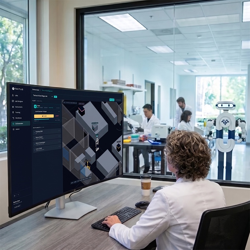 A scientist reviews the Tactus AI orchestration software while a humanoid lab assistant works in the lab beyond the glass