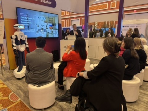 Michael Quick speaks to a seated audience at the CAP26 Tech Talk Theater, with Elsie by Tactus standing beside the stage