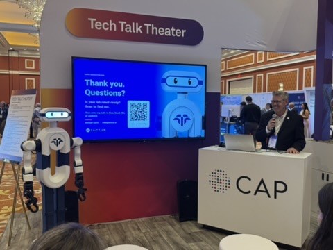 Elsie by Tactus stands beside the CAP26 Tech Talk Theater screen showing "Thank you. Questions?" while Michael Quick takes questions at the podium