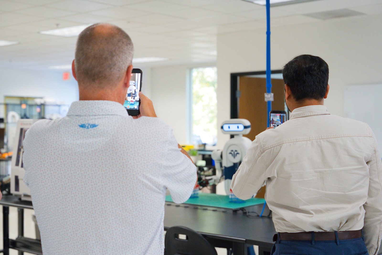 Two guests photograph the Tactus AI humanoid robotic lab assistant with their phones during the Open House